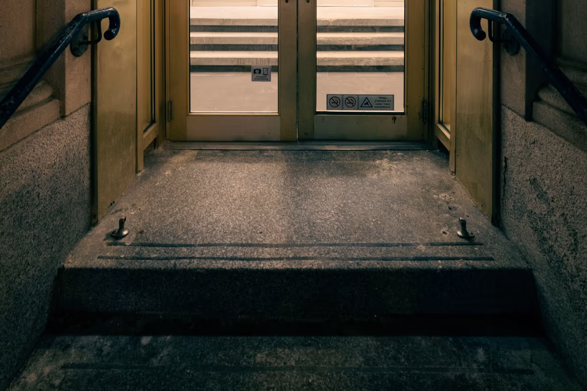 Entrée vitrée d'un établissement recevant du public précédée d'un palier et d'une marche formant un ressaut, mains courantes de part et d'autre