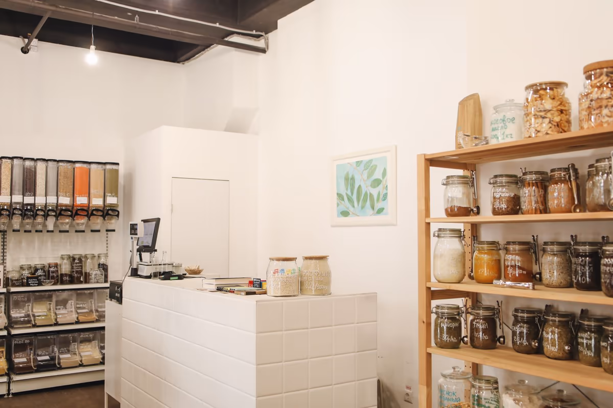 Intérieur d'un petit commerce de détail, comptoir d'encaissement carrelé et circulation entre les rayonnages de bocaux et les distributeurs de vrac