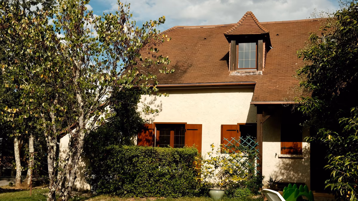 Maison individuelle en crépi clair à toiture de tuiles et lucarne, entourée d'un jardin arboré, dans une commune rurale de Nouvelle-Aquitaine