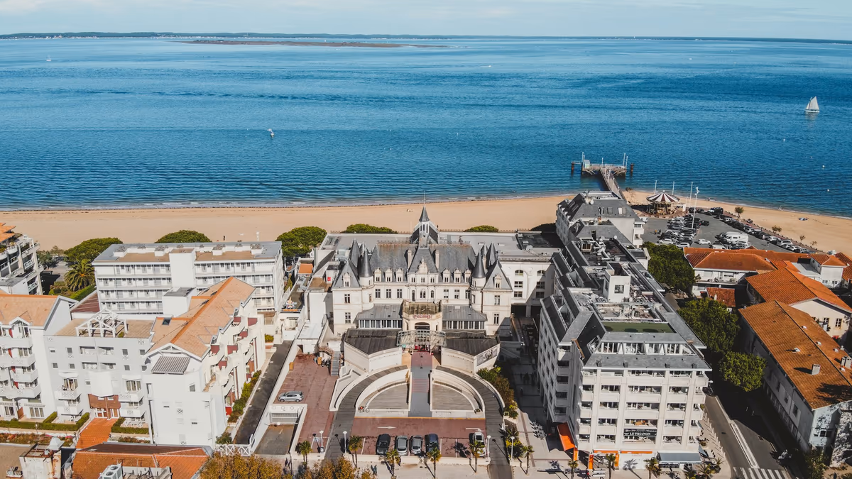 Vue aérienne du front de mer d'Arcachon : bâtiments de première ligne alignés face à la plage et au Bassin, jetée au loin