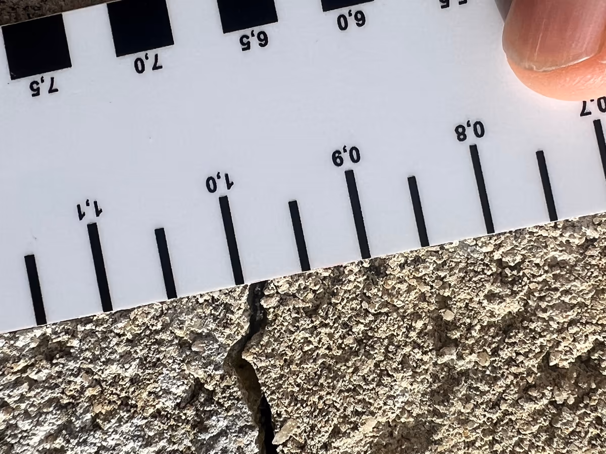 Carte fissuromètre graduée posée en travers d'une fissure d'enduit de façade pour en relever l'ouverture, photo d'expertise