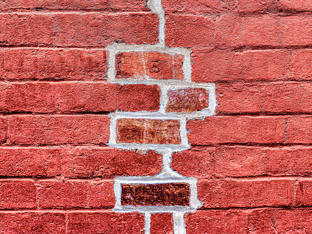 Fissure en escalier sur un mur de briques : le tracé suit les joints de mortier, alternant lits horizontaux et joints verticaux, et contourne les briques sans les traverser