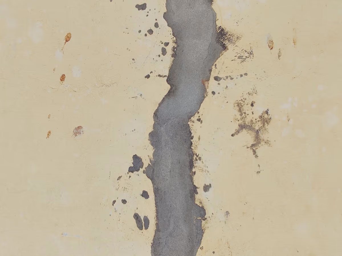 Trace de reprise sur une façade : fissure verticale rebouchée au mortier de ciment gris, tranchant nettement sur l’enduit crème vieilli du reste du mur