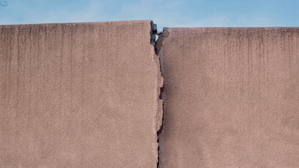 Mur de façade enduit fendu sur toute sa hauteur par une fissure verticale ouverte, les deux lèvres décalées l'une par rapport à l'autre
