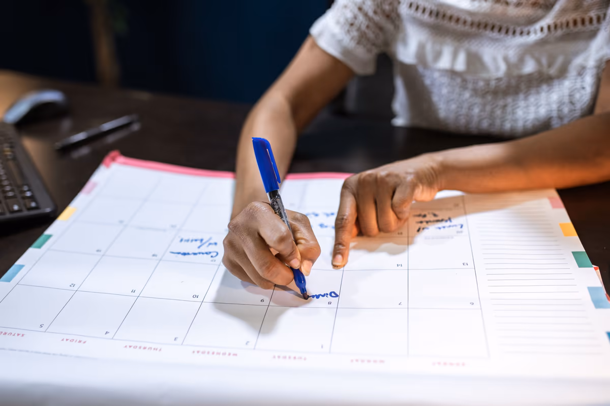 Main inscrivant un rendez-vous au stylo sur un calendrier de bureau, pour fixer la date d'une visite de constat