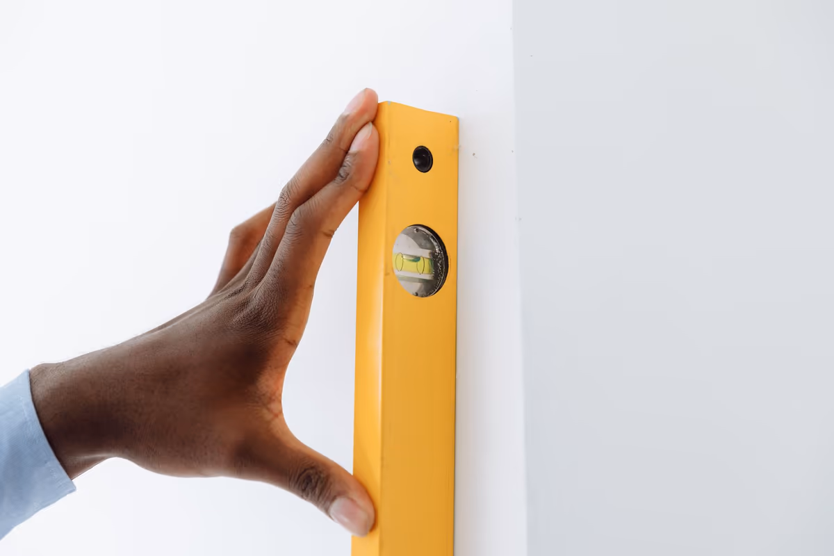Main appliquant un niveau à bulle contre l'arête d'un mur intérieur pour en contrôler la verticalité, la fiole de la bulle lisible au premier plan