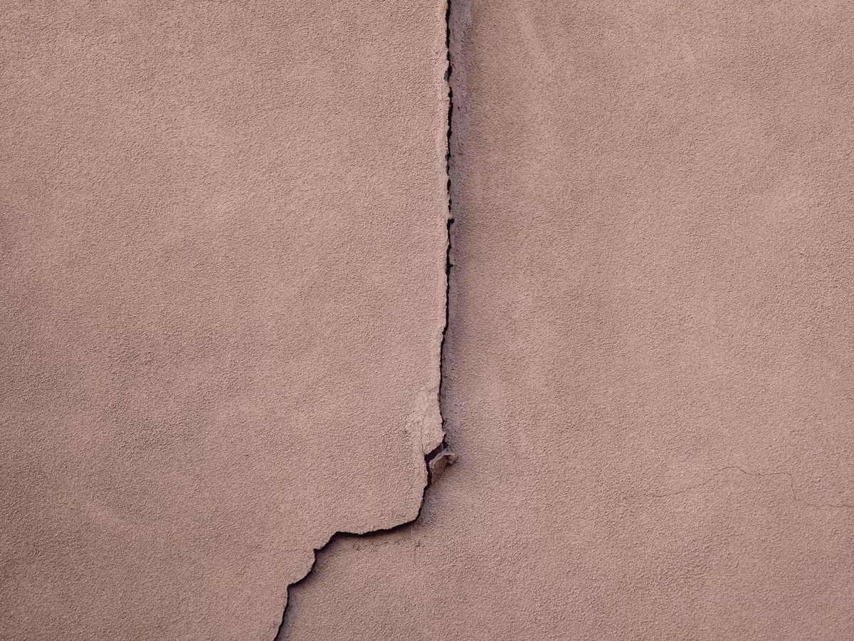 Fissure structurelle traversant l'enduit d'une façade, tracé vertical prolongé vers le bas par une branche oblique qui décroche par ressauts successifs