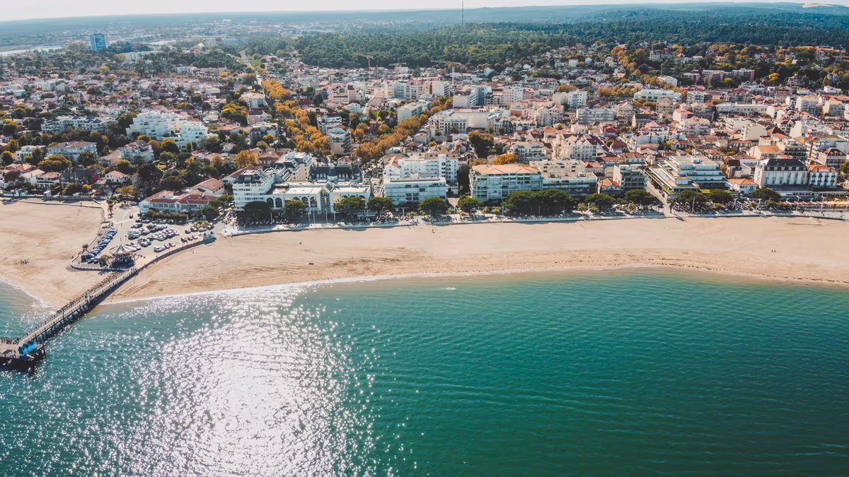 Vue aérienne du front de Bassin à Arcachon : immeubles de première ligne alignés derrière la plage, face à l'eau, jetée à gauche