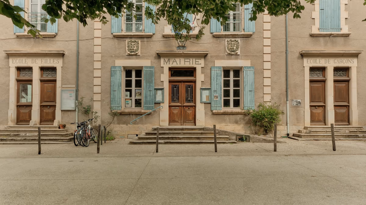 Façade d'une mairie de village française, panneaux d'affichage municipaux encadrant la porte d'entrée sous le mot MAIRIE gravé dans la pierre