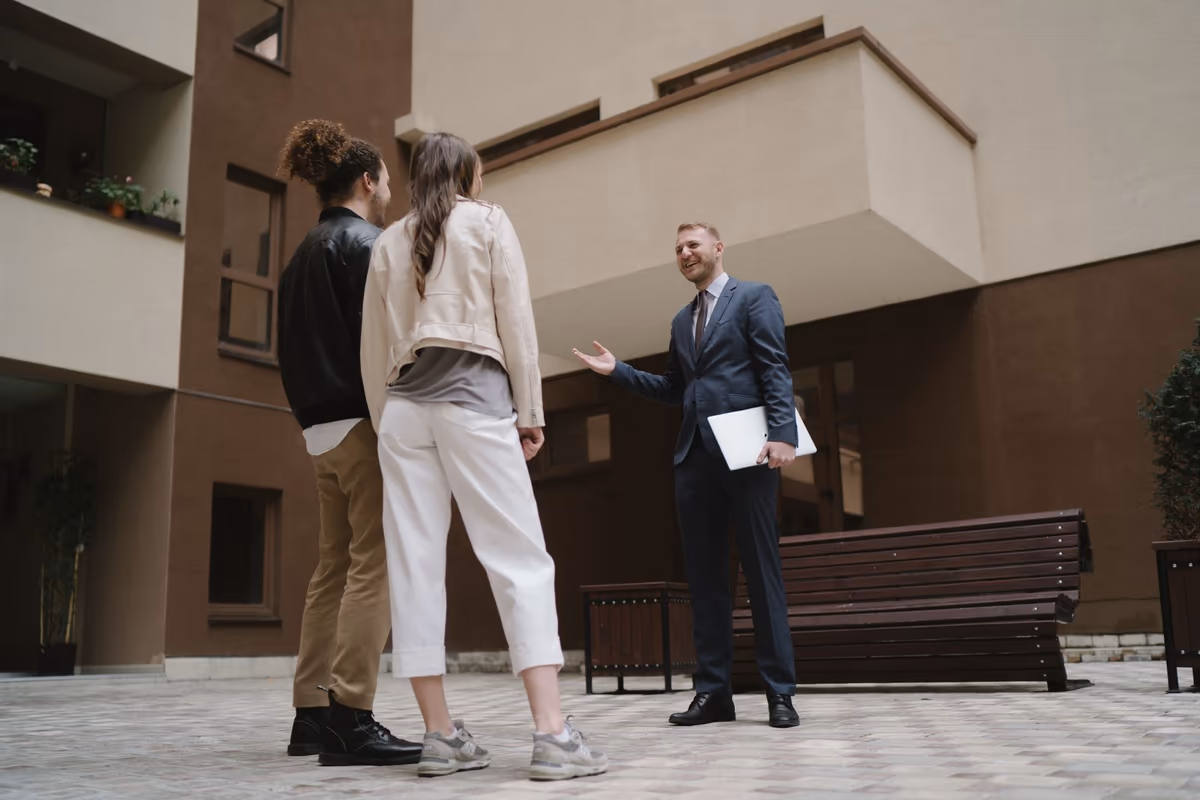 Échange entre occupants et un professionnel en costume, dossier sous le bras, dans la cour pavée d'un immeuble d'habitation en copropriété