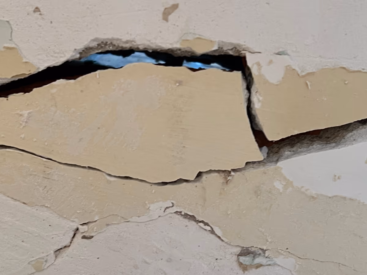 Fissure très ouverte dans un mur, lèvres décalées l'une par rapport à l'autre et enduit éclaté par plaques le long du tracé