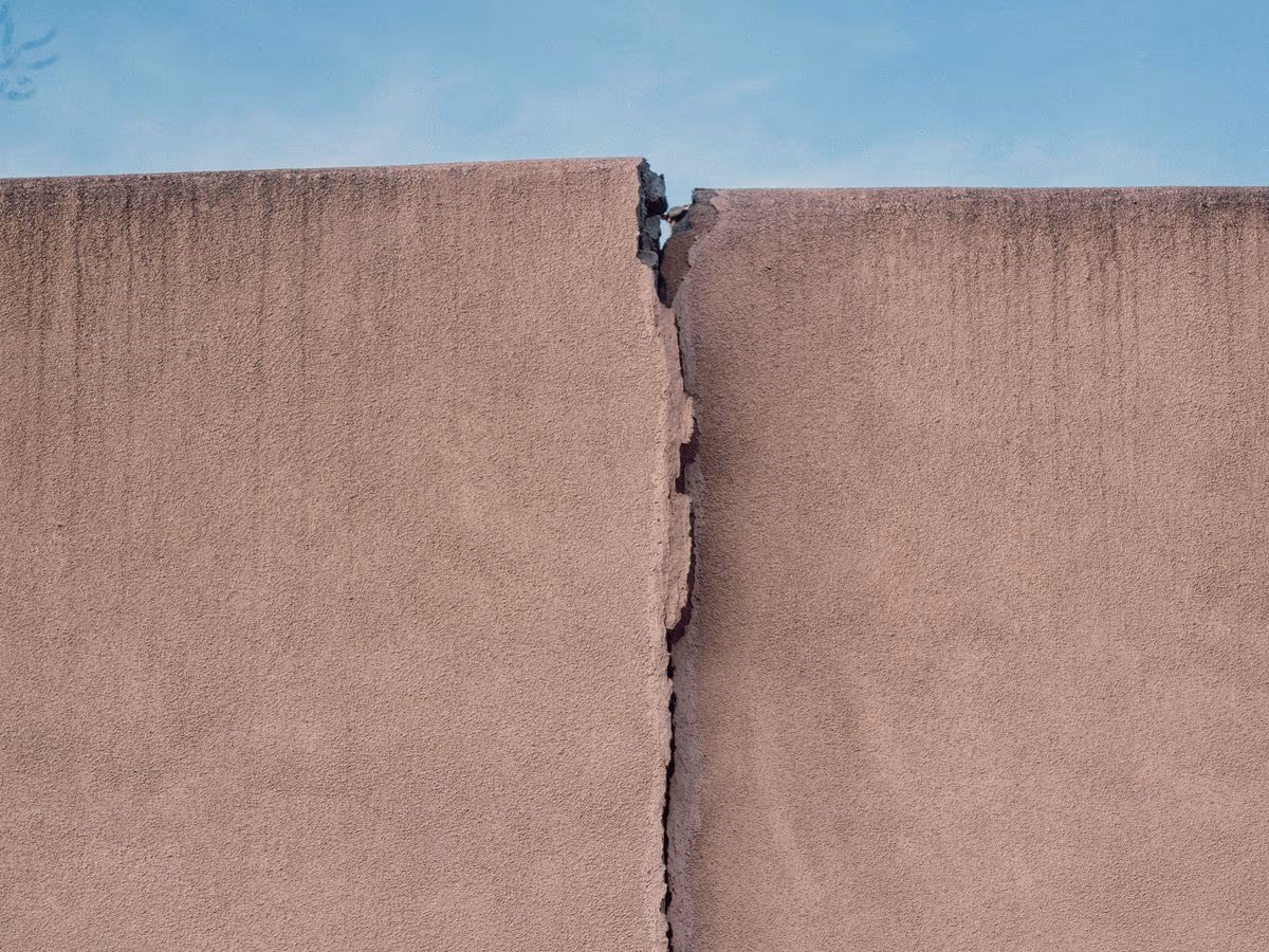 Fissure traversante ouverte de haut en bas dans un mur enduit jusqu'à son arase, avec un décalage net entre les deux lèvres de part et d'autre du tracé