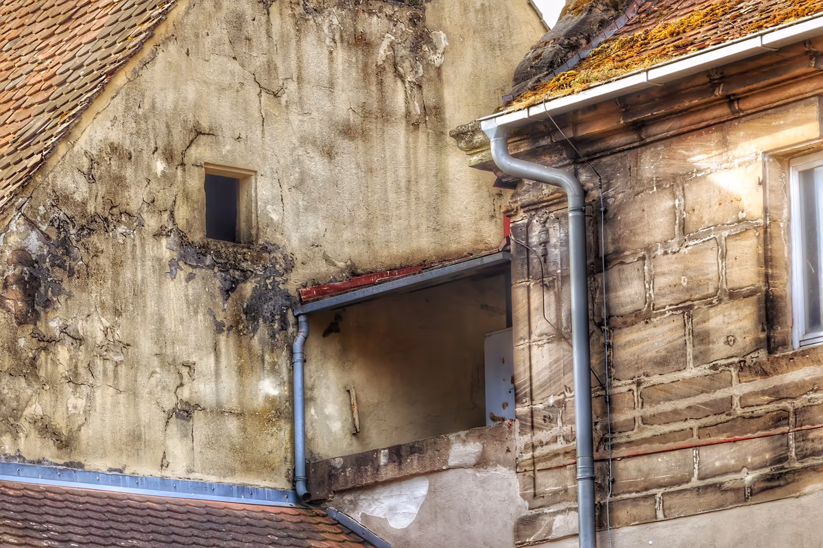 Pignon d'un bâtiment ancien où un enduit fissuré et décollé jouxte un mur en pierre appareillée dont les joints ont été repris à plusieurs époques