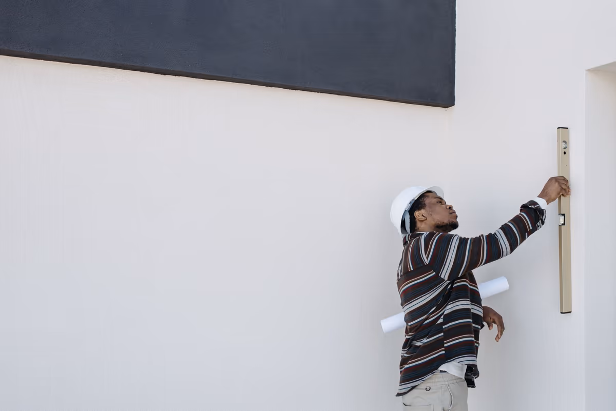 Niveau à bulle appliqué contre l'arête verticale d'un mur de façade, plan roulé sous le bras, pendant un relevé de verticalité sur site