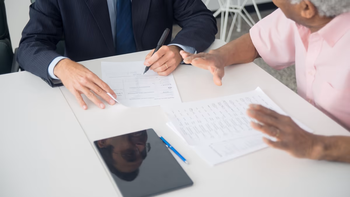 Vue en plongée sur une table où deux personnes travaillent sur le même dossier, l'une annotant un formulaire au stylo, l'autre tenant sa propre copie des mêmes documents