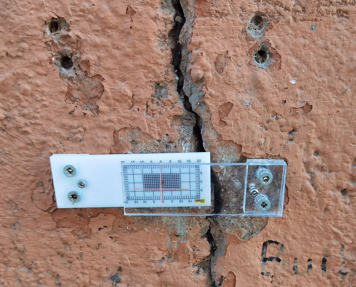 Fissuromètre à deux plaques graduées vissé en travers d'une fissure ouverte dans l'enduit d'une façade, pour suivre l'évolution de son ouverture entre deux relevés