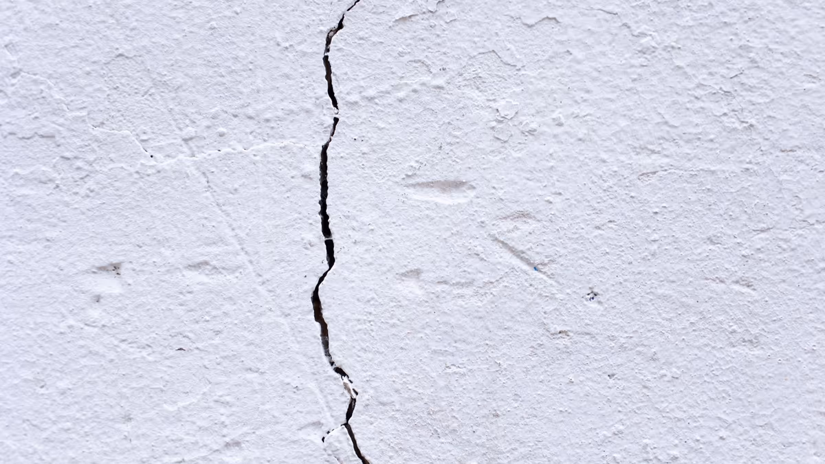 Fissure verticale ouverte traversant l'enduit blanc du mur extérieur d'une maison individuelle