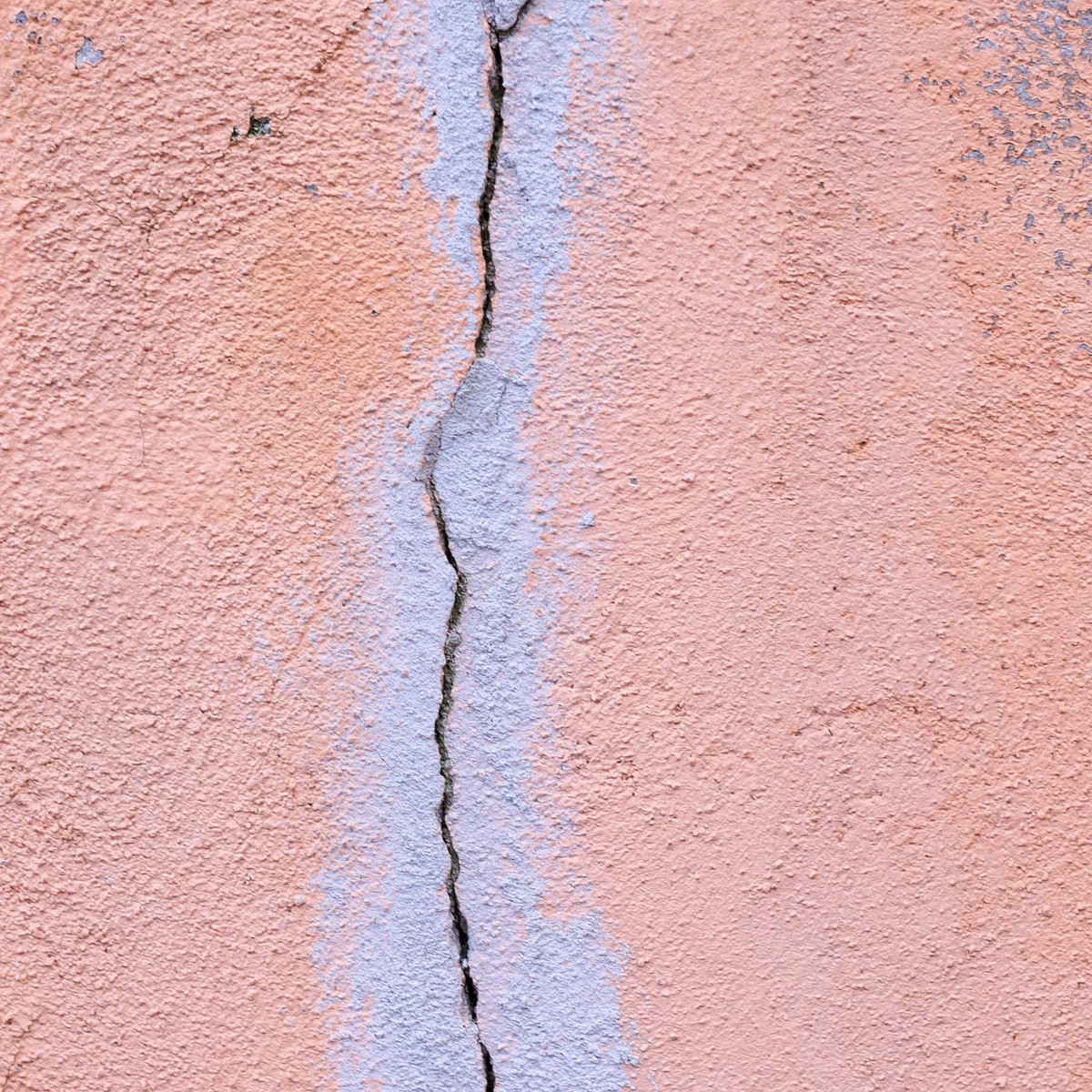 Fissure fine et rectiligne sur un mur de façade enduit, à peine marquée malgré son tracé continu sur toute la hauteur du cadre