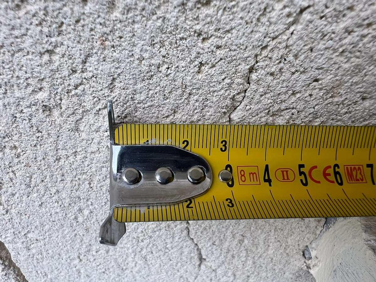 Mètre ruban plaqué sur un enduit de façade en travers d'une fissure fine qui court au-dessus et au-dessous du ruban