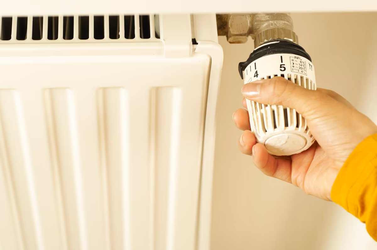 Main actionnant le robinet thermostatique d’un radiateur mural, raccordement et vanne apparents au-dessus de l’appareil
