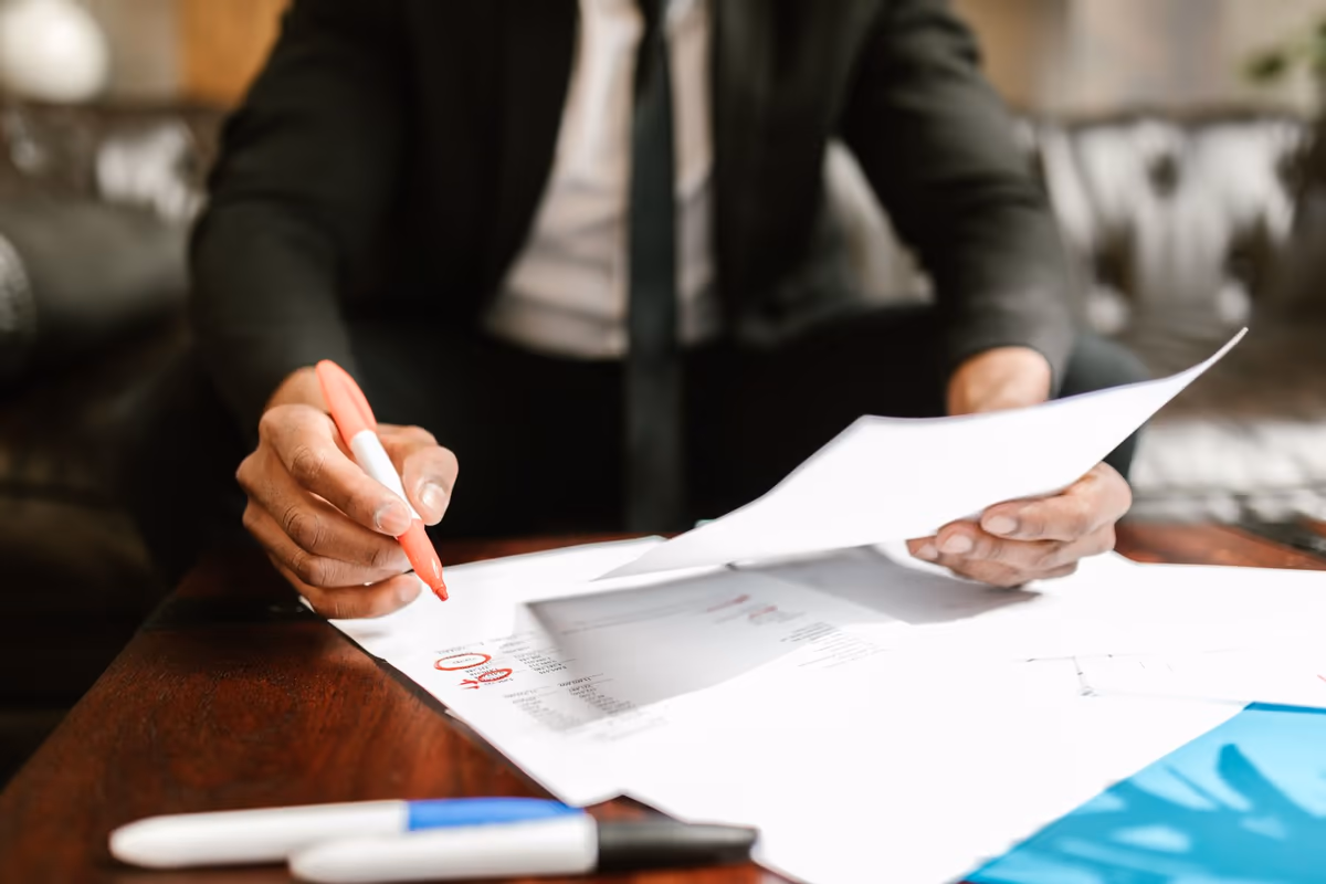Documents de chantier étalés sur une table, une page annotée au feutre et une autre tenue en main, en préparation d’un courrier recommandé à l’entreprise