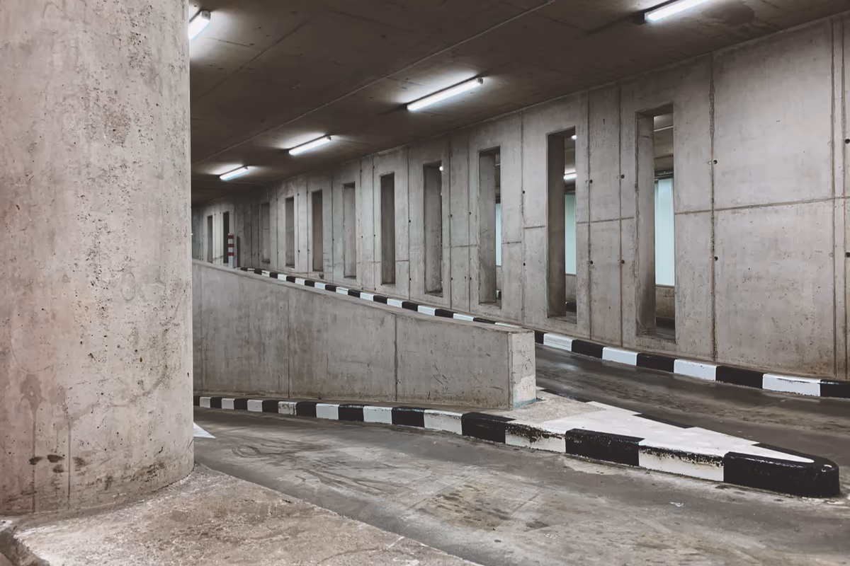 Rampe d’accès en béton desservant les boxes de garage en sous-sol d’un immeuble, bordures marquées et parois sans désordre apparent