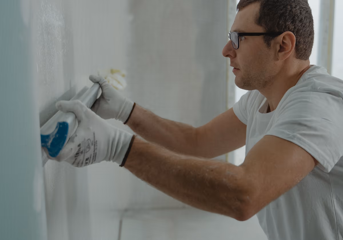 Artisan appliquant un enduit au couteau sur un mur intérieur en plaques de plâtre, pendant la reprise d’un désordre après réception