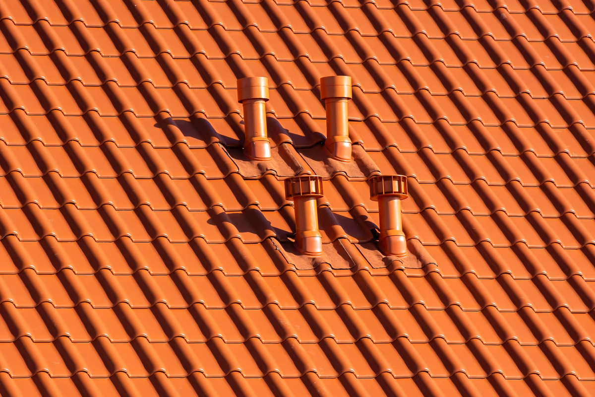 Quatre sorties de ventilation traversant une couverture en tuiles mécaniques, avec les tuiles découpées et les collerettes d'étanchéité autour de chaque passage