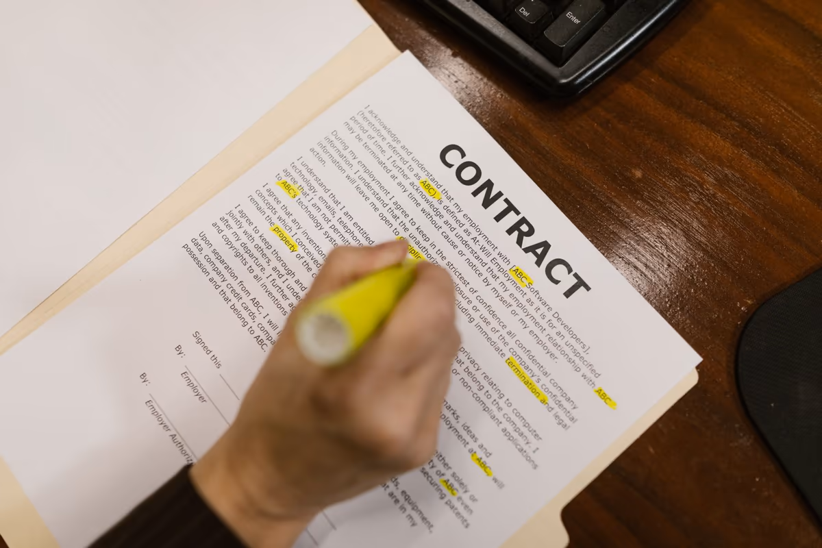 Contrat d'assurance ouvert sur un bureau, plusieurs passages du corps de texte surlignés au marqueur jaune, main tenant le surligneur
