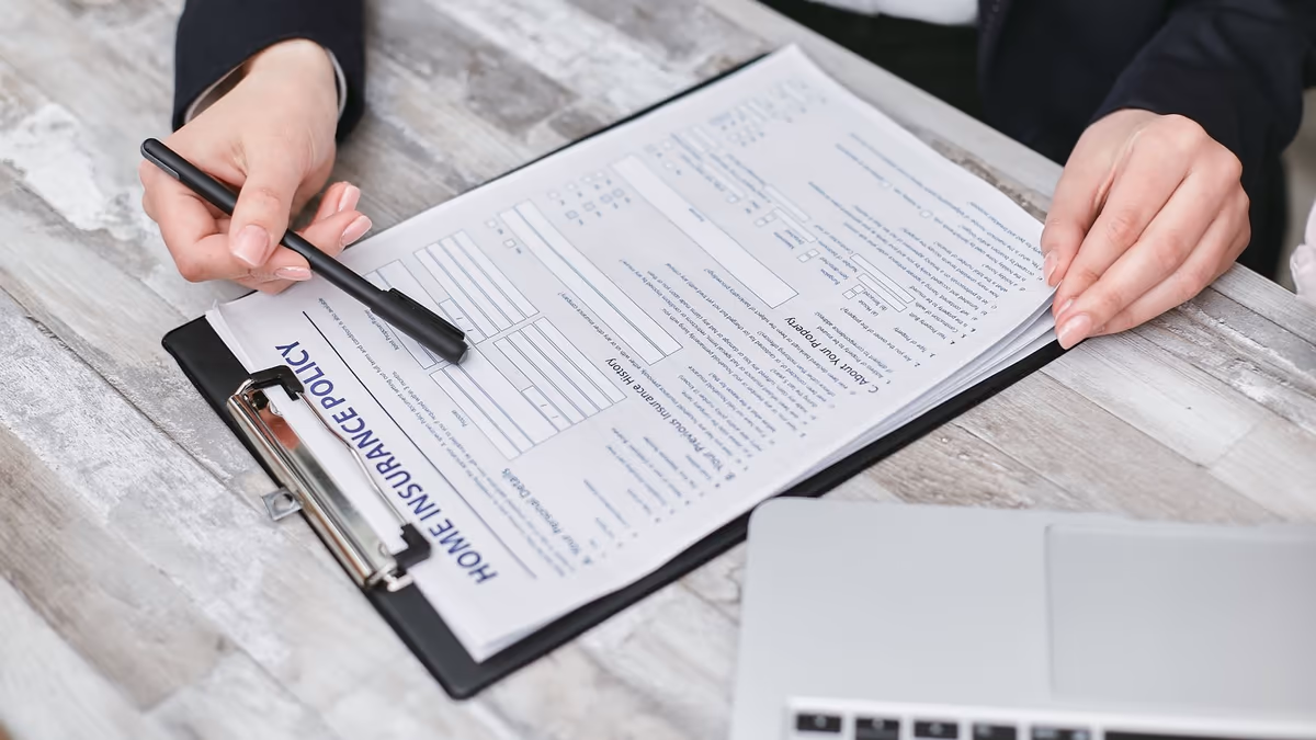 Contrat d'assurance habitation posé sur un porte-bloc et relu page à page, stylo en main, après un sinistre