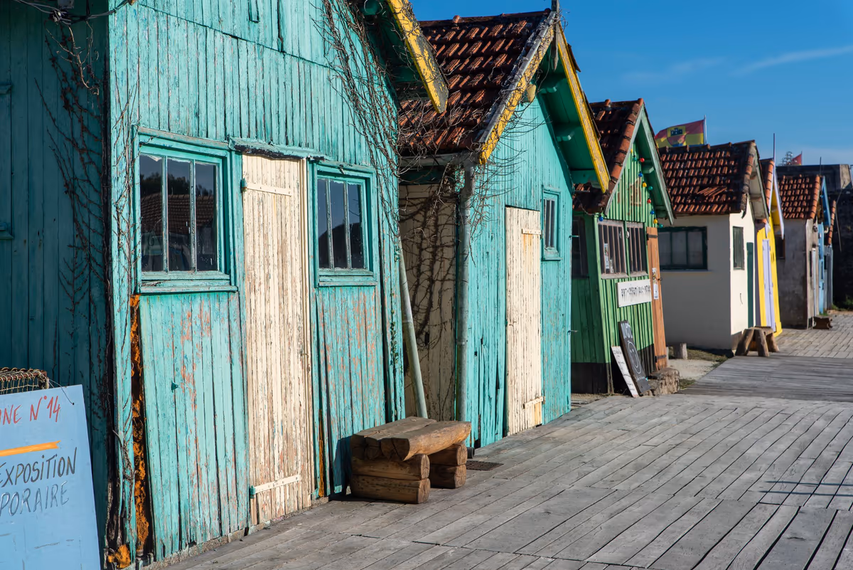 Cabanes en bois peint alignées sur un ponton en planches : lames verticales grisées, peinture qui s'écaille surtout en bas des portes et du bardage
