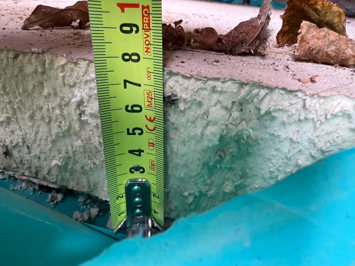 Mètre ruban posé à la verticale contre la tranche d'une dalle coulée sur un isolant, au-dessus d'un film plastique