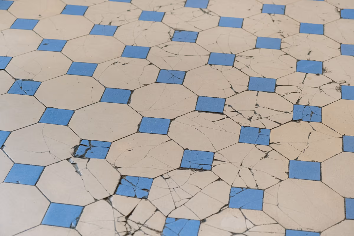 Carrelage de sol à motif octogonal parcouru de fissures qui traversent plusieurs carreaux et franchissent les joints