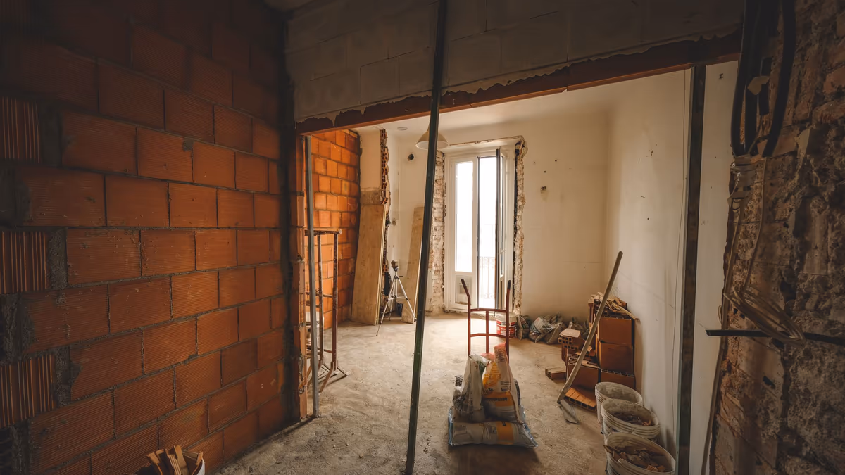 Pièce de maison en cours de travaux, cloison de briques montée sans enduit et sacs de mortier au sol, chantier laissé en l’état