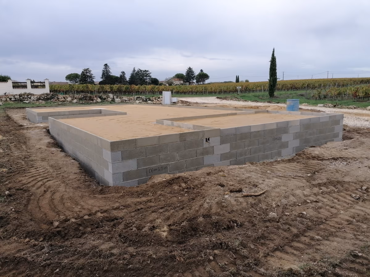 Soubassement d'une maison neuve monté en blocs béton et rempli de sable compacté, en attente du dallage, sur un terrain terrassé