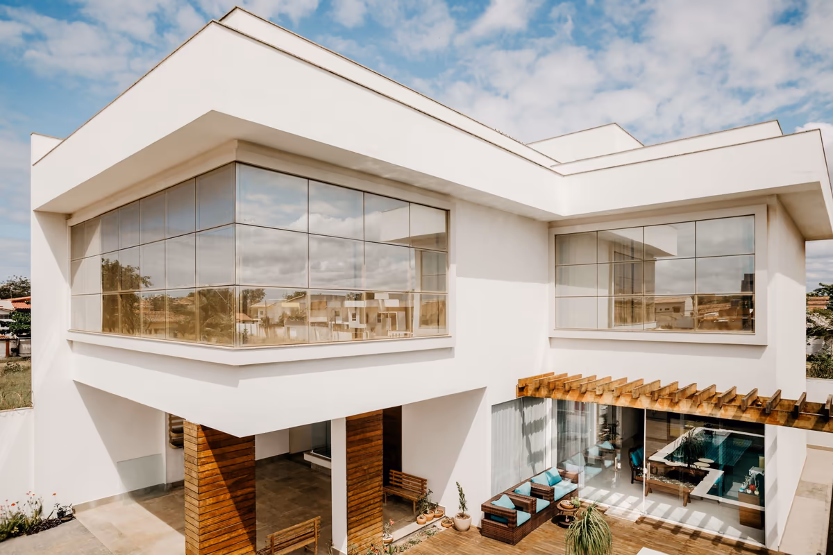 Façade de maison contemporaine dont les baies vitrées sont abritées par un débord de dalle formant casquette à l'étage, et par un brise-soleil en lames de bois au-dessus de la terrasse du rez-de-chaussée
