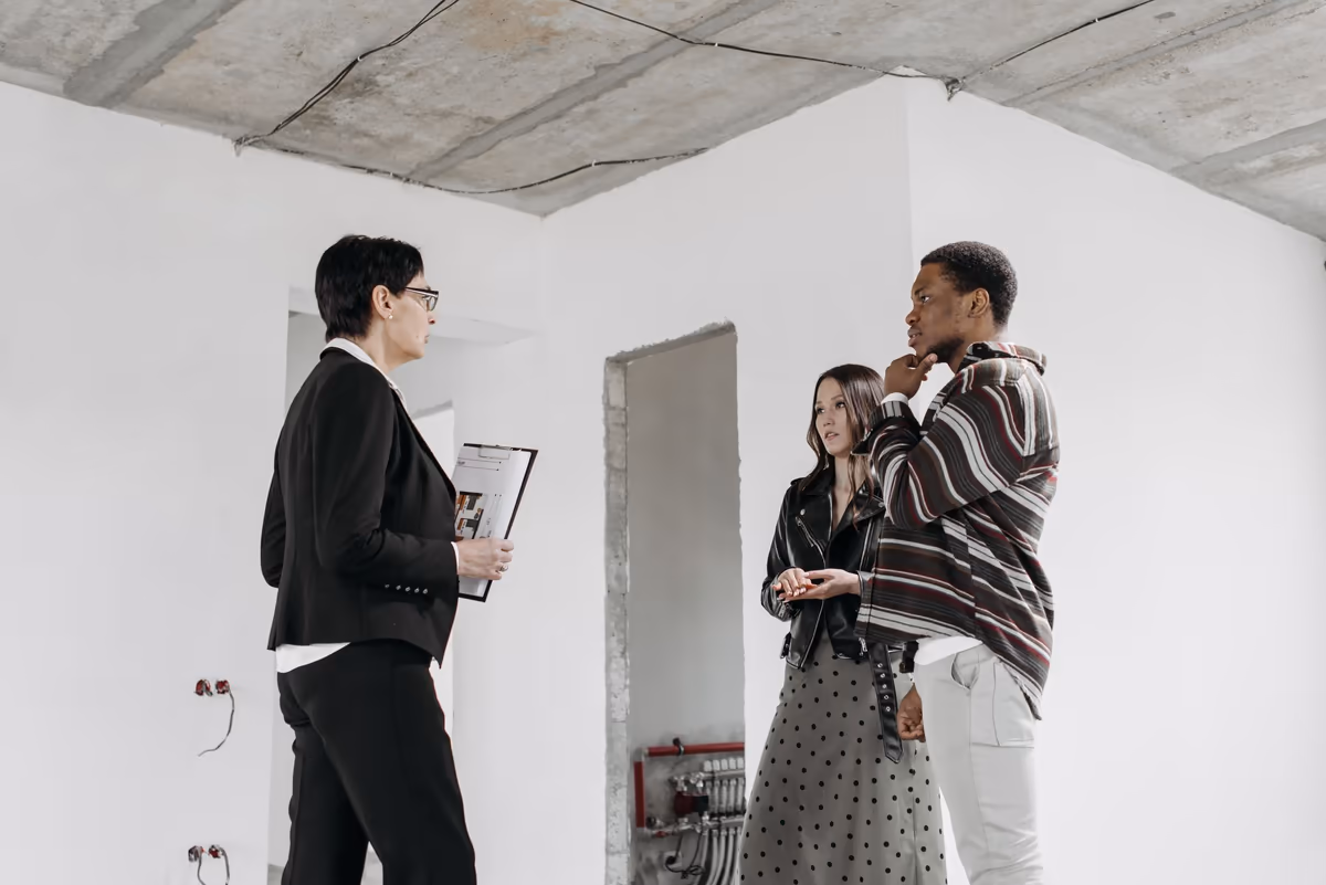 Professionnelle tenant un porte-bloc face à un couple de propriétaires, debout dans une pièce dont les travaux ne sont pas achevés