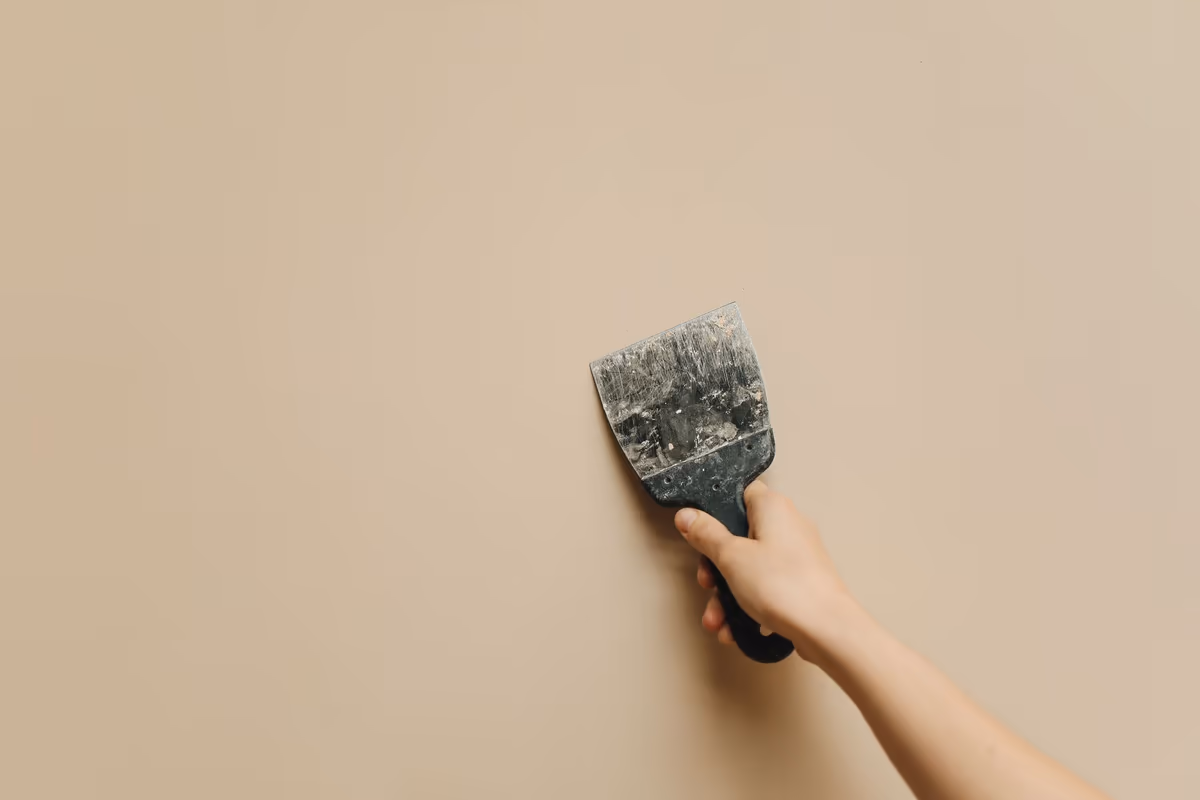 Main tenant une spatule à enduire appliquée contre un mur intérieur uni, pendant la reprise d’une finition de peinture