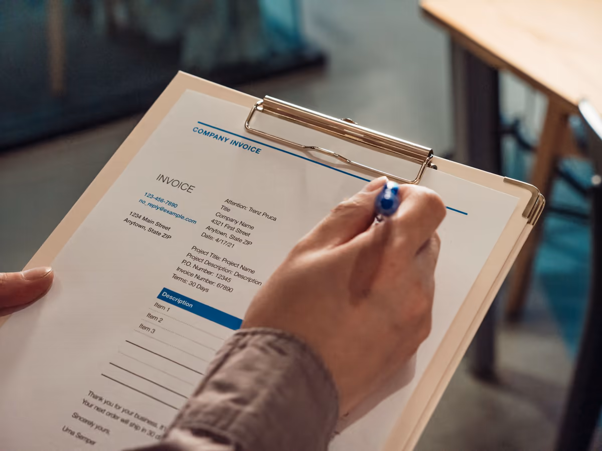Main tenant un stylo au-dessus d'un document chiffré fixé sur un porte-bloc, les lignes de postes détaillées visibles sous l'en-tête