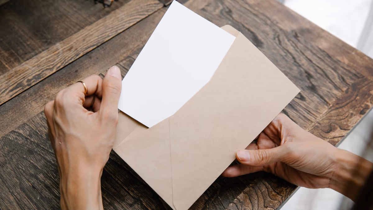 Deux mains sortent une lettre d'une enveloppe kraft posée sur une table en bois, vue de dessus