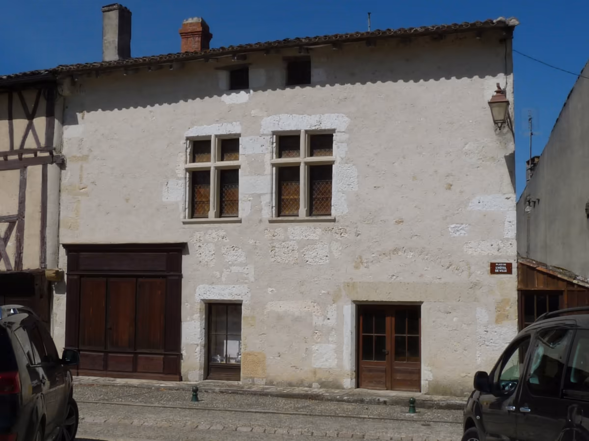 Maison ancienne en pierre calcaire à Gensac, en Gironde : façade sur rue où des pierres plus claires signalent des reprises autour des baies, accolée à une maison à pans de bois d'une autre époque