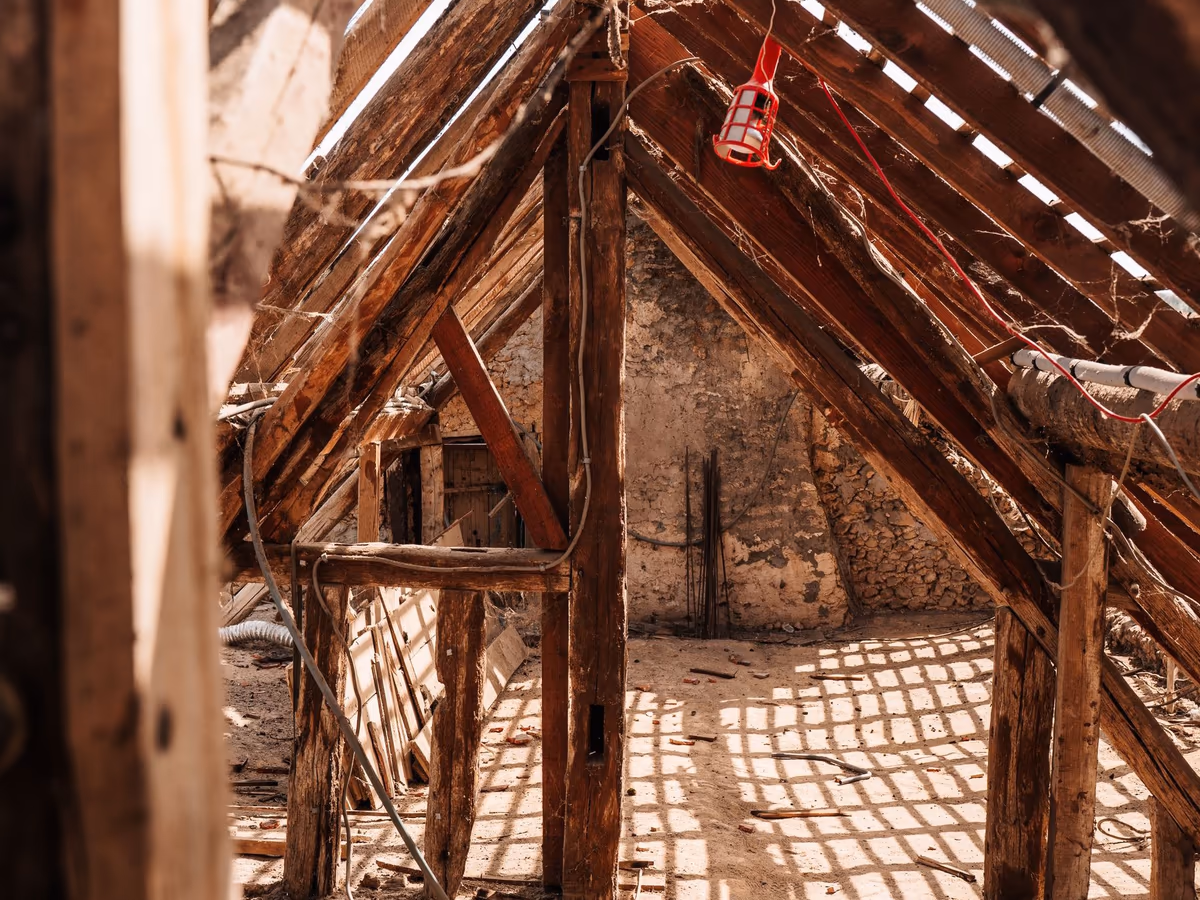 Comble d'une maison ancienne mis à nu : poteaux et arbalétriers en bois posés sur un mur de maçonnerie, voliges et lattis apparents sous la couverture