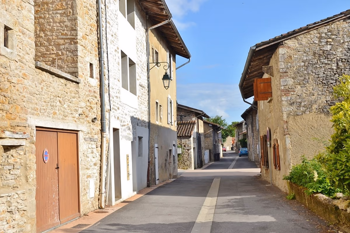 Rue d'un bourg ancien bordée de maisons en pierre calcaire, façades mitoyennes, volets bois et rez-de-chaussée ouvrant directement sur la voirie
