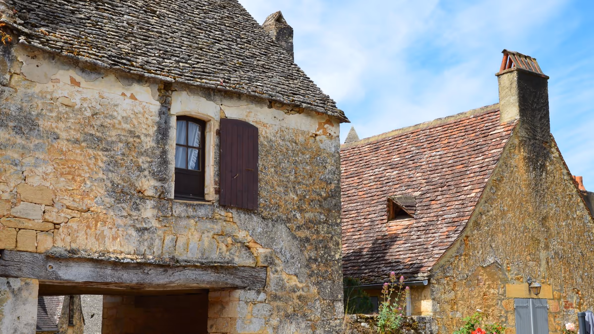 Maisons de bourg en pierre calcaire aux toitures de lauzes et de tuiles anciennes, façades mitoyennes sous un ciel dégagé