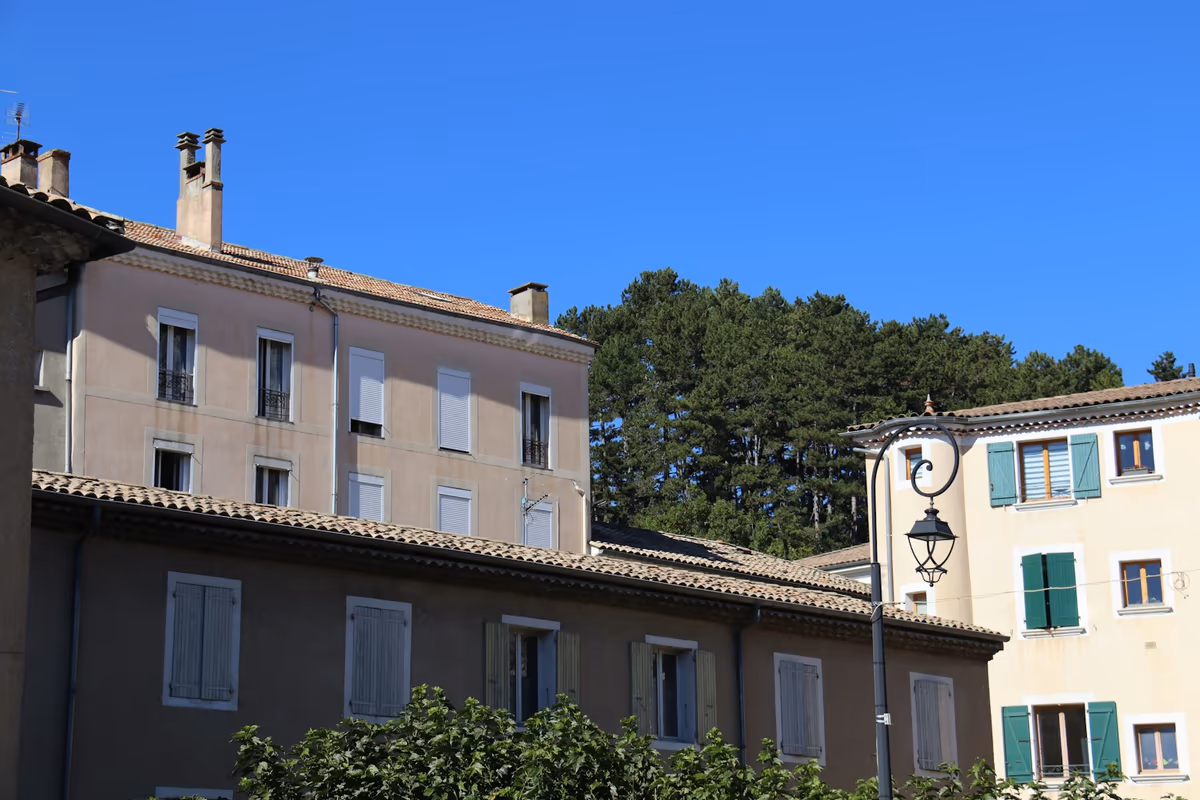 Immeubles d'habitation anciens à toitures en tuiles, souches de cheminées, façades enduites et volets, sous un ciel dégagé