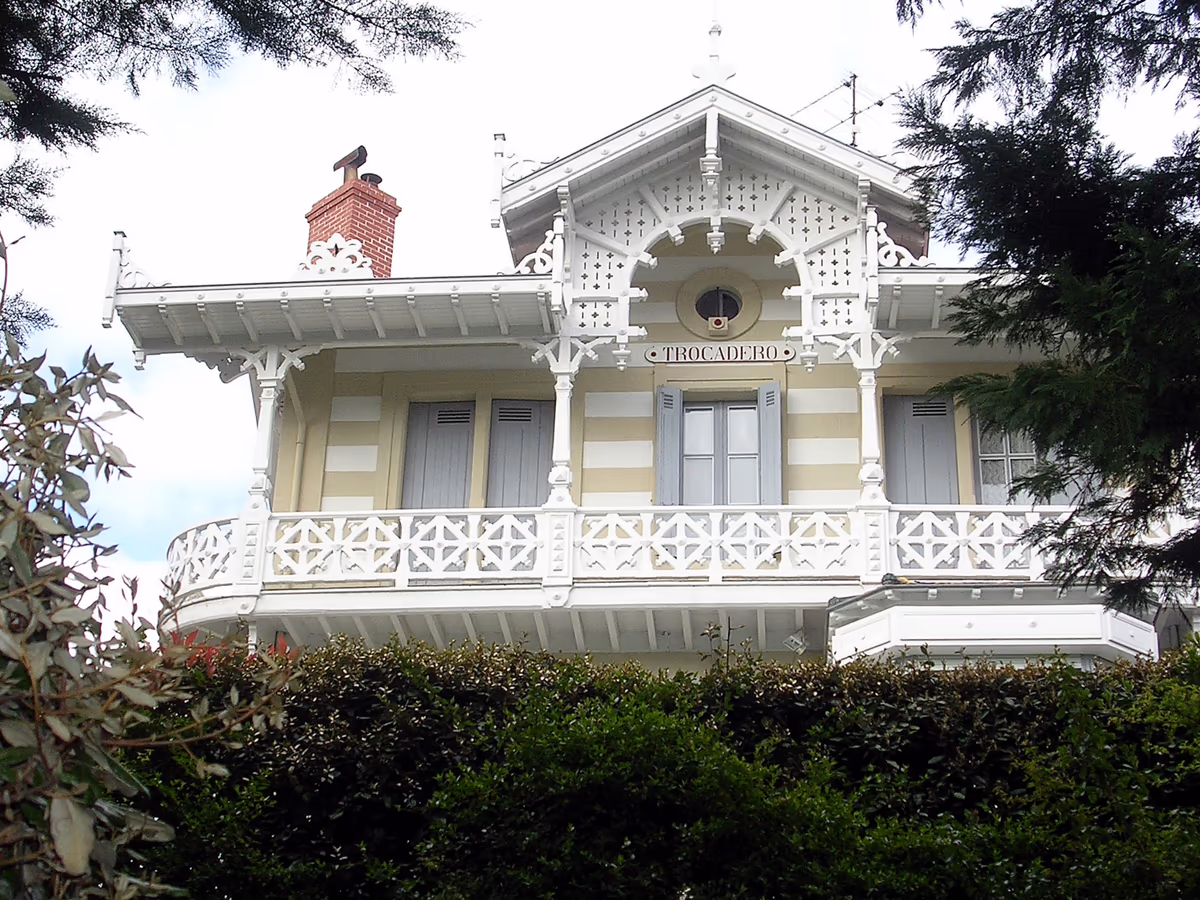 Balcon en bois découpé de la villa Trocadéro à Arcachon : garde-corps ajouré, poteaux, consoles et lambrequins ouvragés peints en blanc, sous un pignon décoré